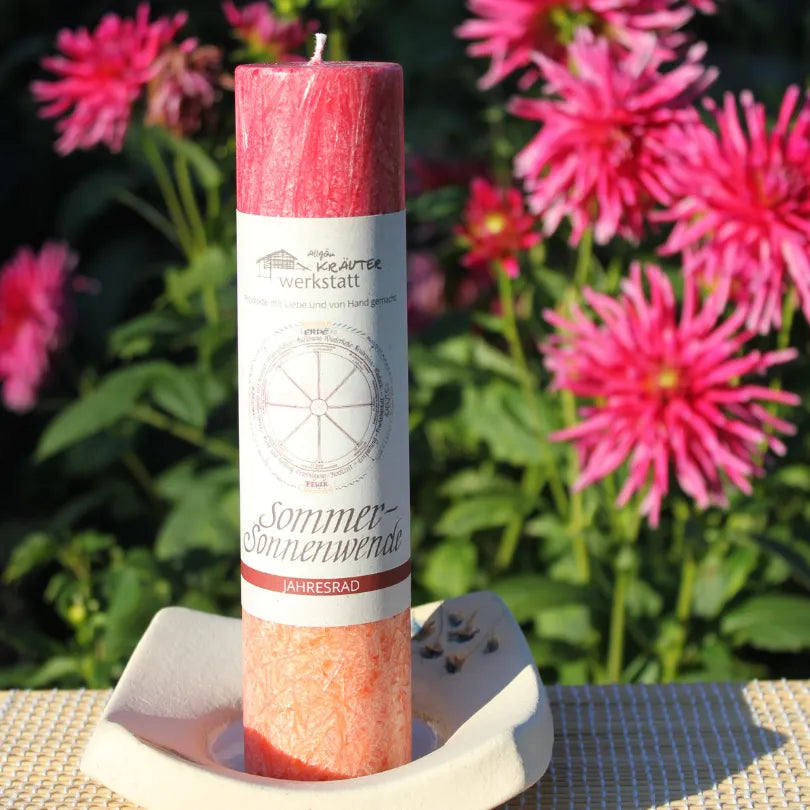 Rot-orange Kräuterkerze "Sommersonnenwende" auf Kerzenteller vor Blüten, ideal für Rituale & innere Reife.