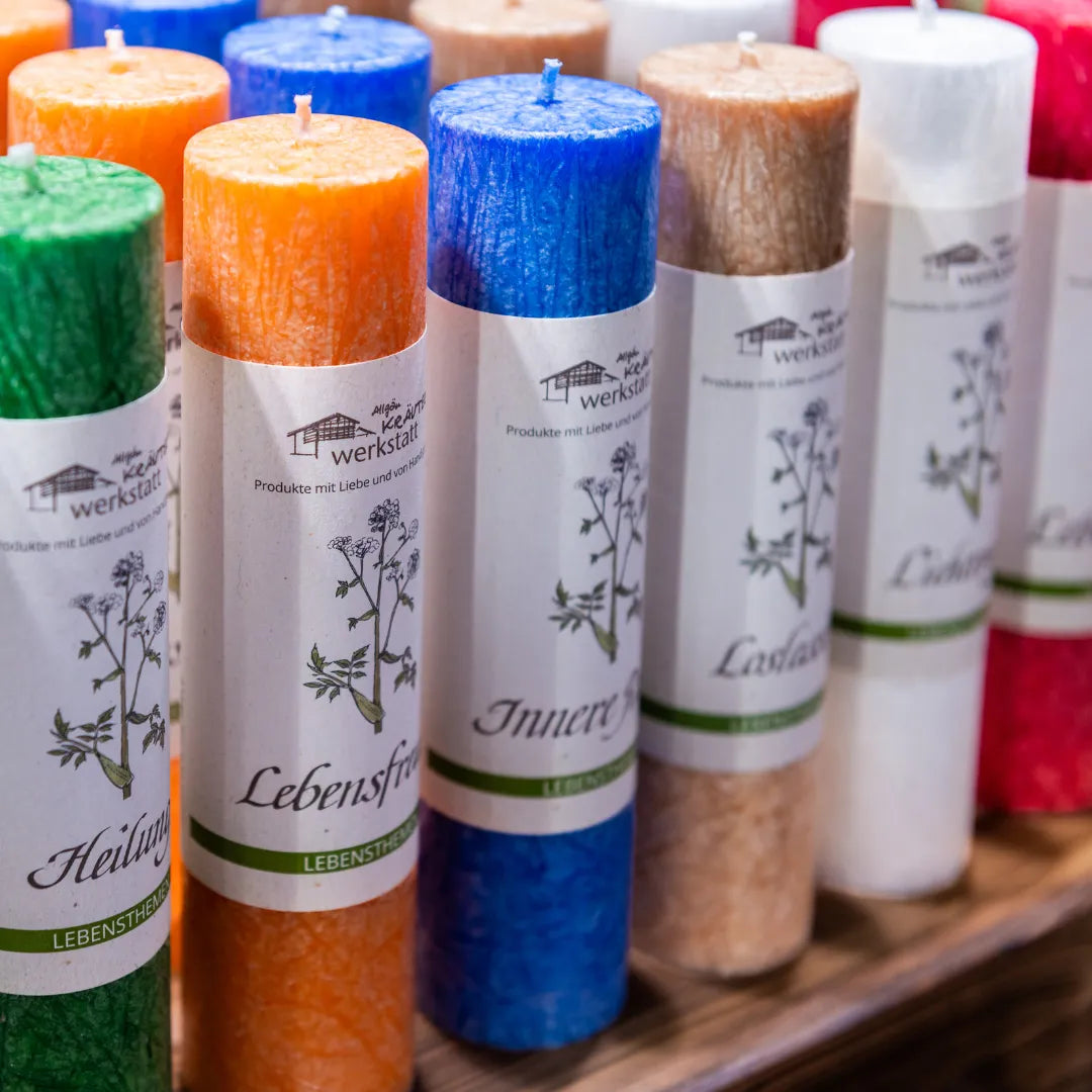 Reihe bunter Allgäuer Heilkräuterkerzen mit Etiketten, die Namen wie "Lebensfreude" und "Innere Ruhe" zeigen.