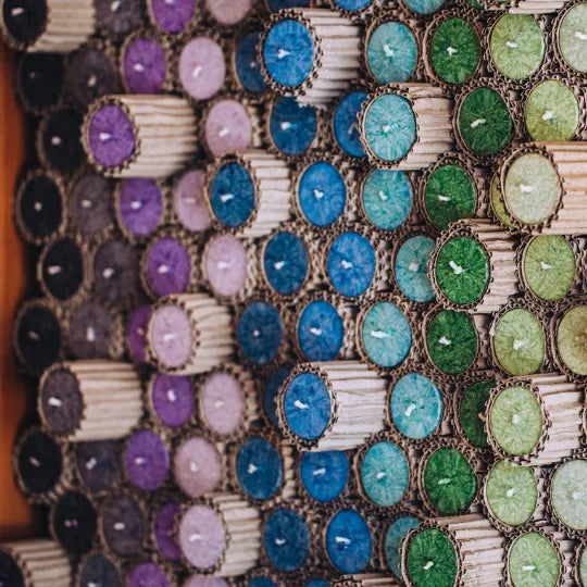 Schrägansicht eines großen Stapels bunter Allgäuer Heilkräuterkerzen in Wellpappe-Hüllen.