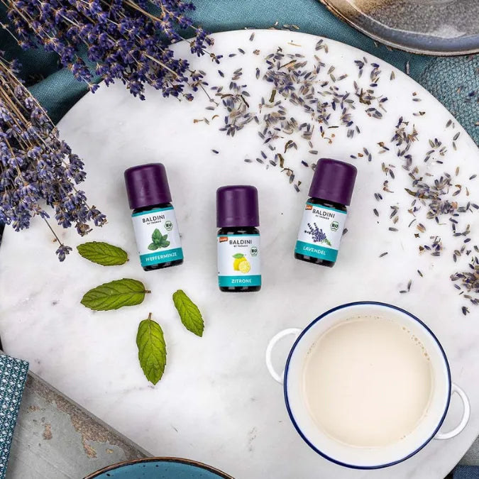 Baldini Bio ätherische Öle: Pfefferminze, Zitrone, Lavendel auf Marmorplatte mit Lavendelblüten.