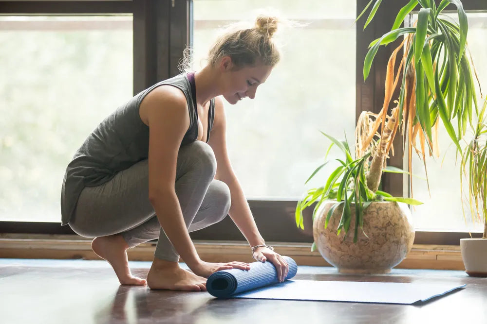 Frau rollt Yogamatte für Progressive Muskelentspannung und innere Ruhe zusammen.
