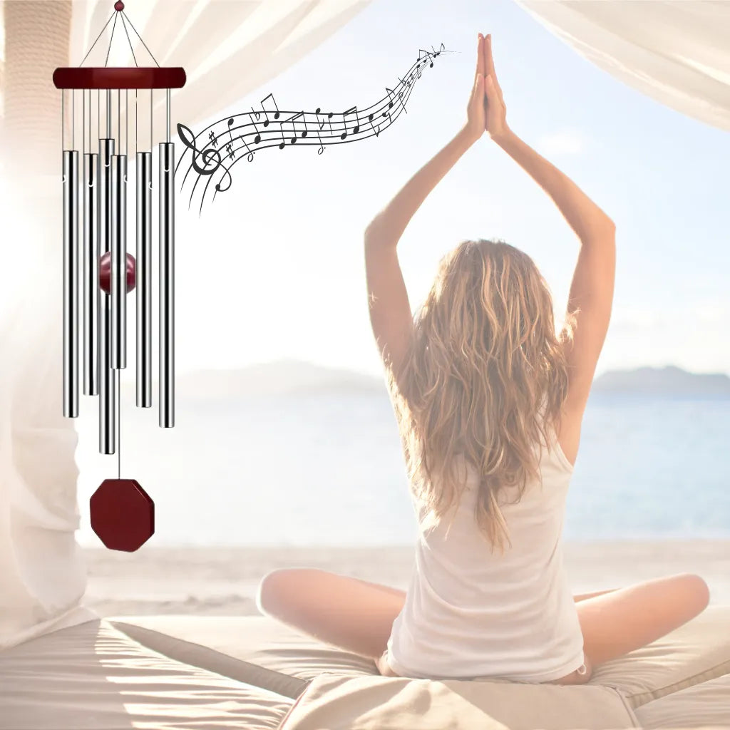 Windspiel mit Notenlinien, symbolisiert Ruhe und Entspannung bei meditierender Frau am Strand.