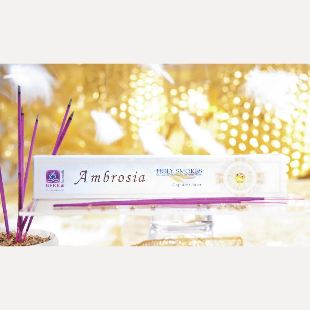 BERK Holy Smokes Ambrosia Räucherstäbchen in violetter Farbe, dekorativ arrangiert mit Packung und Federn.