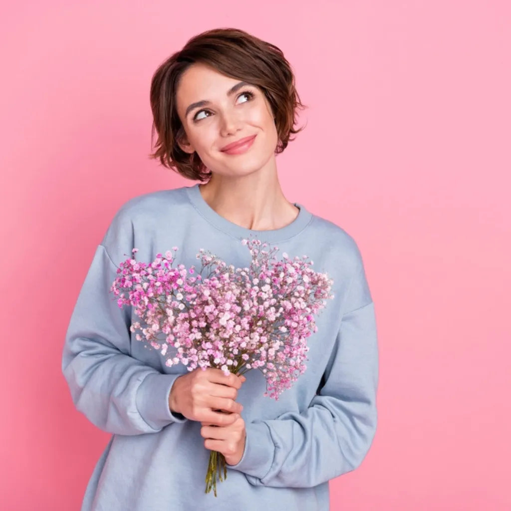 Frau mit Blumenstrauß lächelt, symbolisiert Selbstliebe, Freude und emotionale Unabhängigkeit.