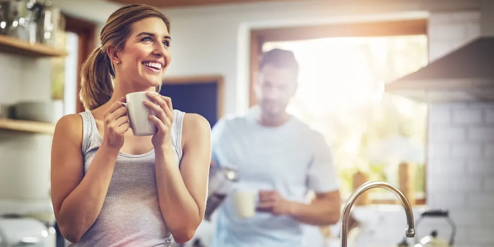 Frau steht mit ihrem Morgen-Kaffee in der Küche und freut sich