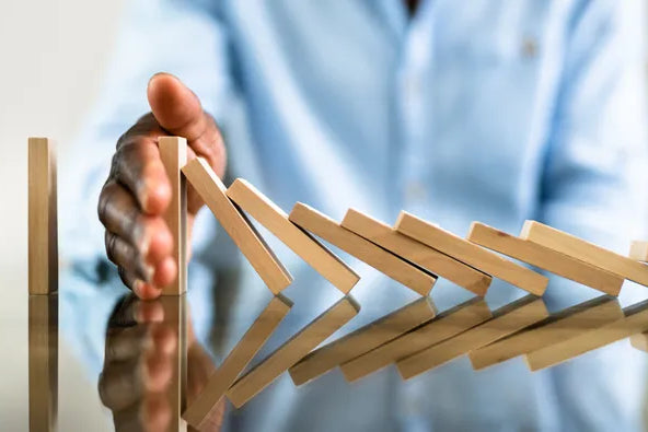Eine Hand stoppt eine Reihe fallender Dominosteine, symbolisierend das Setzen von Grenzen, Krisenmanagement oder das Verhindern negativer Kettenreaktionen.