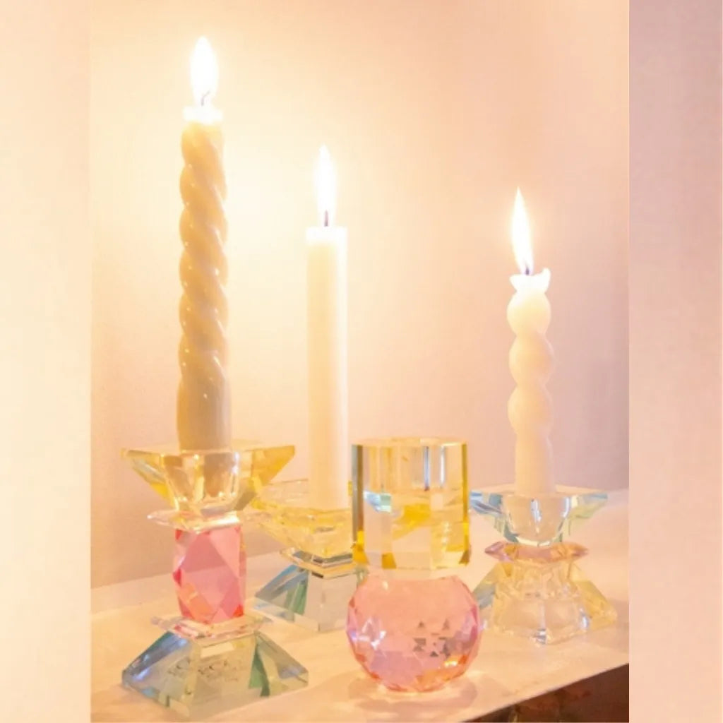 Ansammlung von bunten facettierten Kristall-Kerzenhaltern mit brennenden Stumpen- und Stabkerzen, stimmungsvolle Beleuchtung.