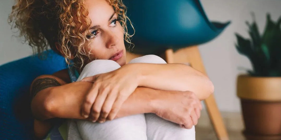 Frau kauert nachdenklich und traurig auf ihrem sofa