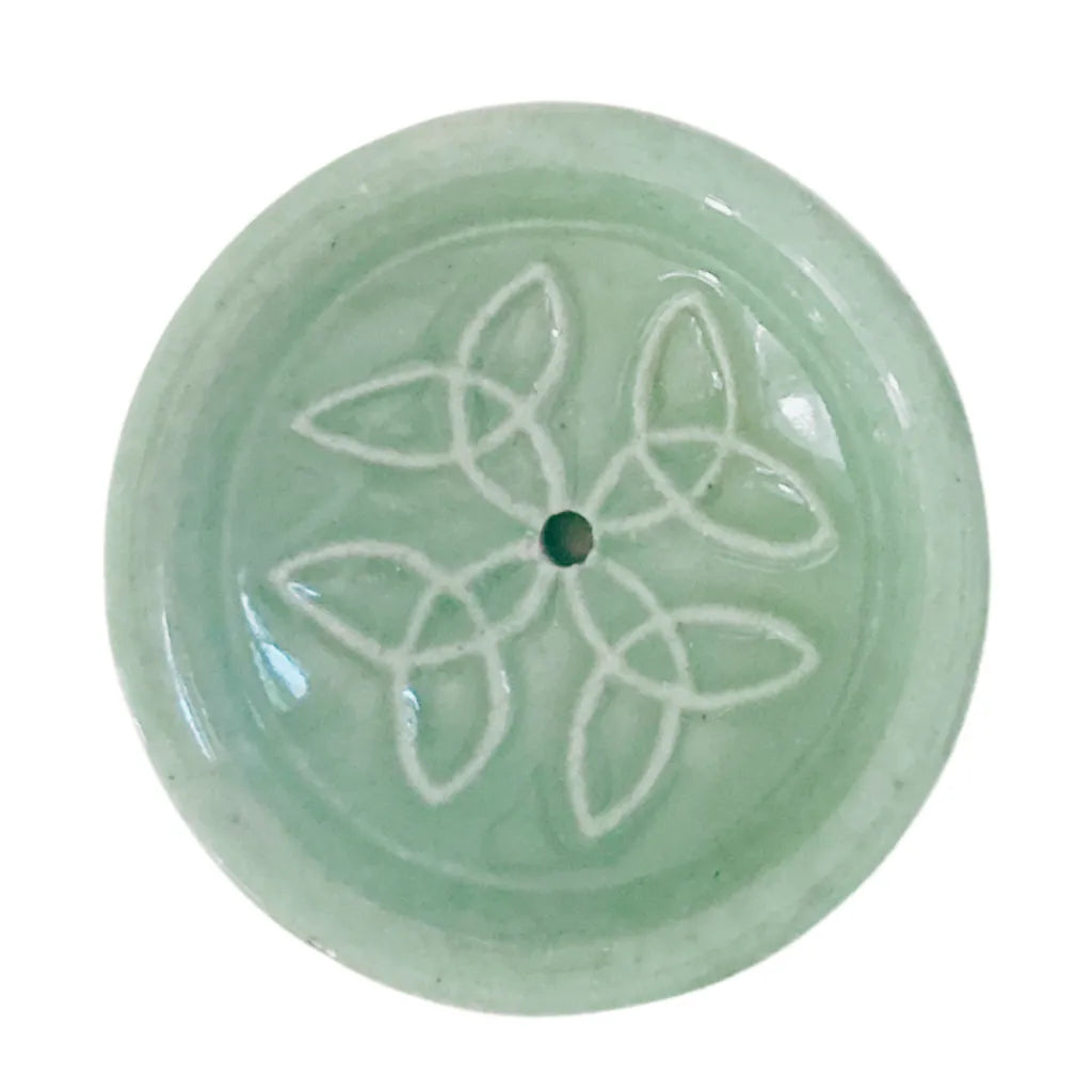 Nahaufnahme eines runden Keramik Räucherstäbchenhalters in sanftem Mintgrün, verziert mit einem harmonischen weißen Knotenmuster und einem zentralen Loch für Räucherstäbchen.