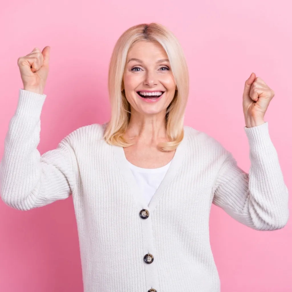 Frau jubelt vor rosa Hintergrund, symbolisiert gestärktes Selbstbewusstsein & Freude durch Selbstliebe.