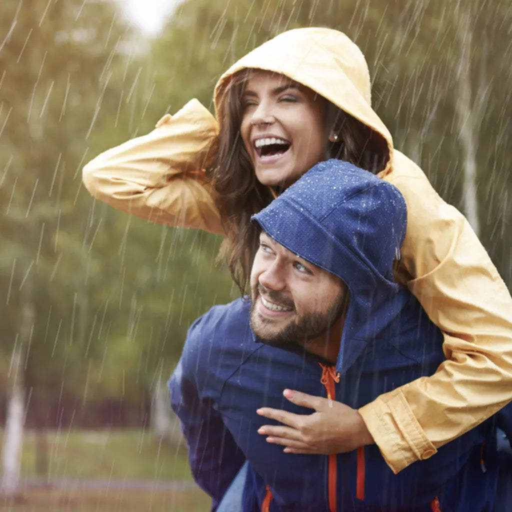Paar lacht fröhlich im Regen, symbolisiert Wohlbefinden & Stärke durch Selbstheilung & Immunsystem.
