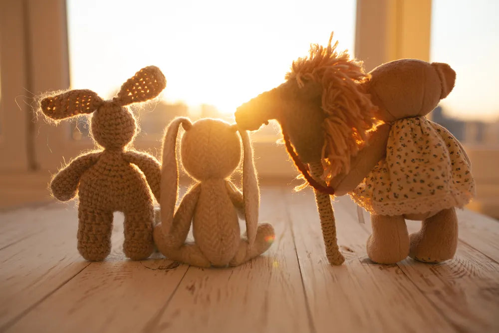 Drei gehäkelte Stofftiere (Hase, Hase, Bär) stehen im Sonnenlicht, symbolisieren Verbundenheit.
