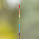 Die Glaskette "Regenbogen" hängt vor einem weichen, unscharfen Hintergrund. Die bunten Glasröhrchen fangen das Licht ein und erzeugen ein harmonisches Farbenspiel, das eine fröhliche Atmosphäre schafft.
