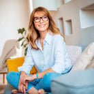 Frau lächelt entspannt auf Sofa, symbolisiert innere Ruhe, Klarheit & Vertrauen durch Intuition.