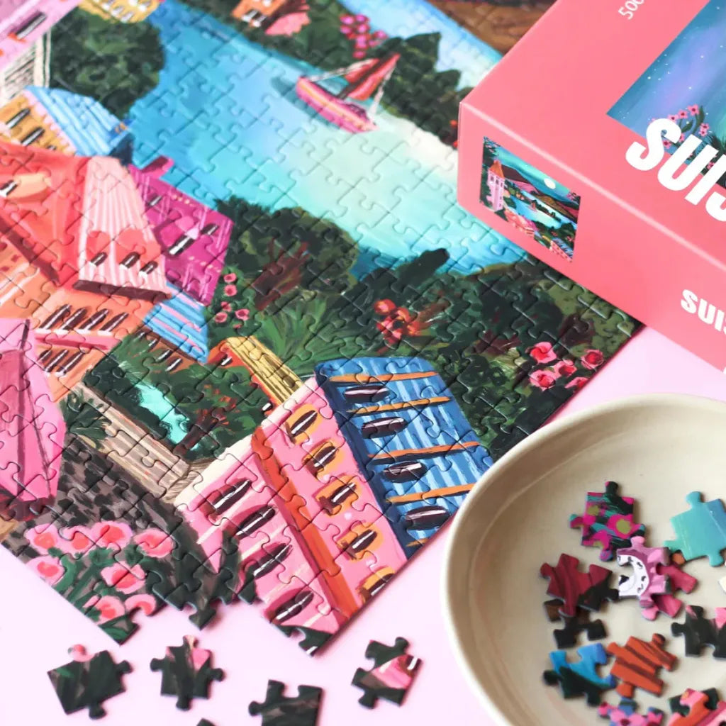 Ein begonnenes Piecely Puzzle 500 "Suisse Nights" mit lose liegenden Puzzleteilen und einer kleinen Schale voller weiterer Teile. Zeigt den Prozess des Puzzelns mit dem Motiv der Schweizer Nacht.