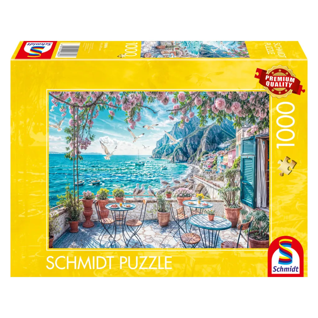 Schmidt Puzzle 1000 Teile "Terrasse am Meer" Produktverpackung. Zeigt ein idyllisches Küstenmotiv mit Balkon, Meer und blühenden Blumen.
