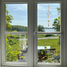 Elegante Sonnenfänger-Kette mit goldenem Lotus & Kristallprismen im Fenster. Bringt Glanz, Ruhe & positive Energie in den Raum.