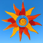 Der orange-gelbe Sonnenfänger Sonne aus Glas mit 15cm Durchmesser hängt vor einem strahlend blauen Himmel. Das Licht scheint durch das farbige Glas und erzeugt brillante Reflexionen.